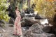 A woman in a long dress standing by a stream.