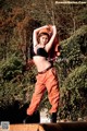 A woman in a black bra top and orange pants posing for a picture.